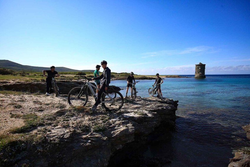 Eine Gruppe Radfahrer auf einer felsigen Küste, im Hintergrund ein Turm. 3