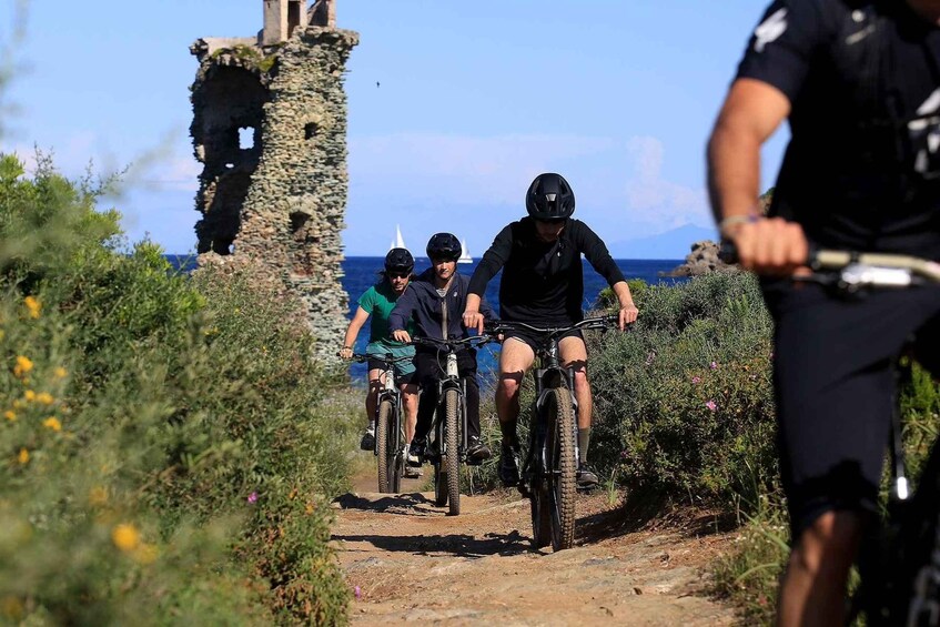 Eine Gruppe von Mountainbikern auf einem unbefestigten Weg, im Hintergrund ein historisches Steingebäude. 5