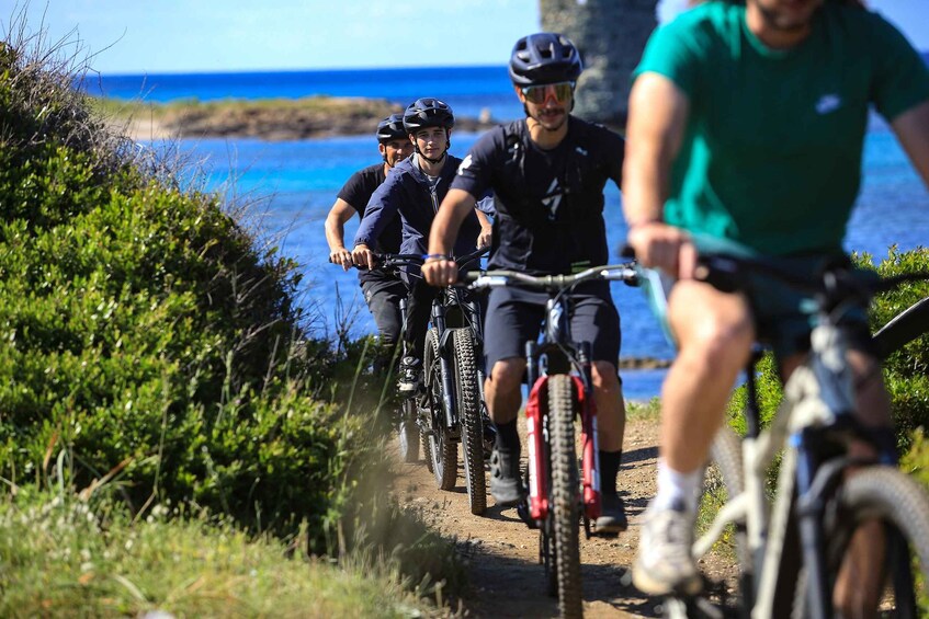 Eine Gruppe Radfahrer auf einem unbefestigten Weg, im Hintergrund das Meer. 2