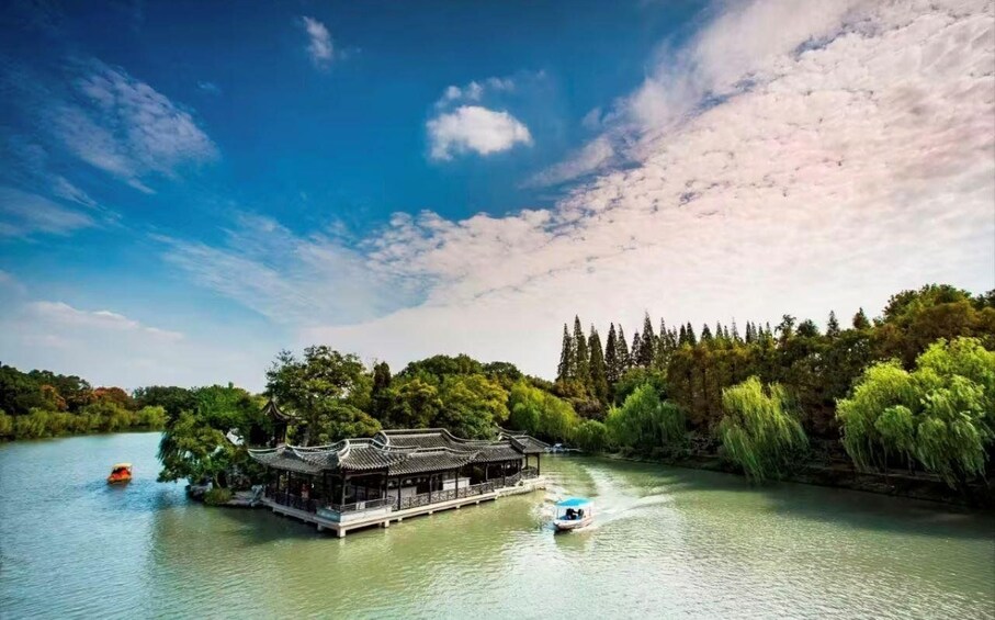 A traditional Chinese pavilion on a river, surrounded by lush greenery and a clear blue sky. 1