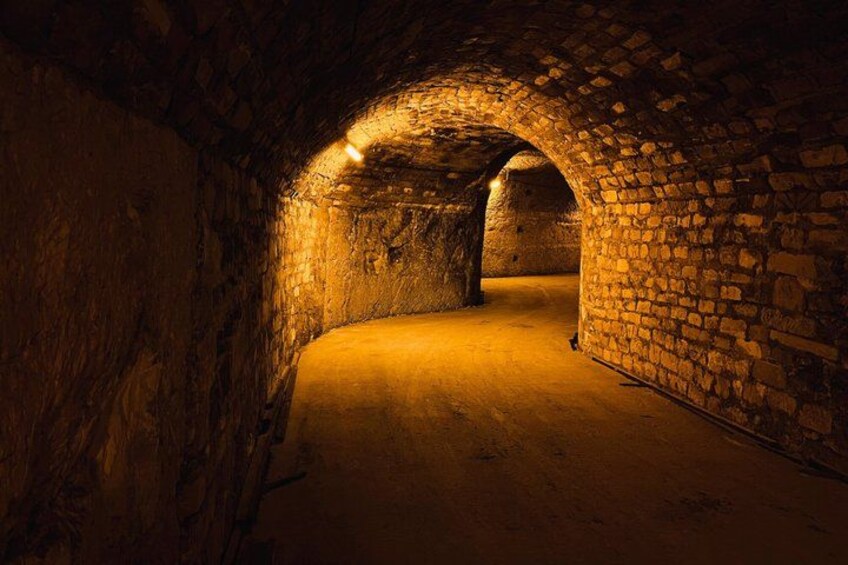 A stone tunnel with arched ceilings and a warm light source. 2