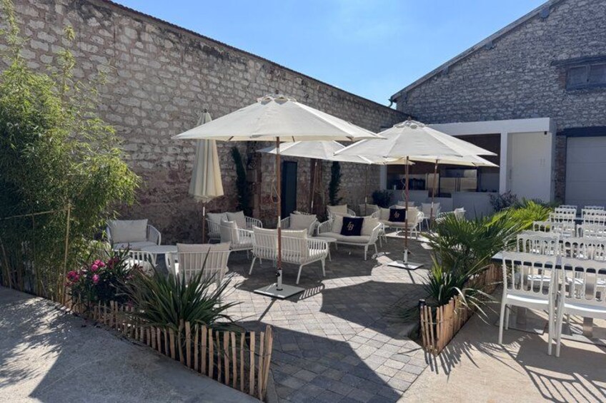 An outdoor patio with white furniture and umbrellas, surrounded by stone walls and plants. 4