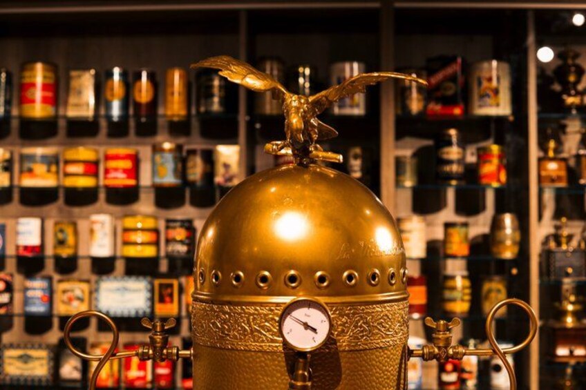 A brass distillation apparatus with a gauge, surrounded by shelves of various bottles. 5