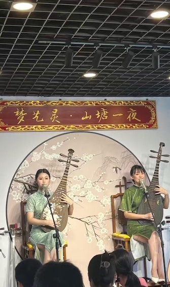 Två musiker uppträder på scen med traditionella instrument, en dekorativ bakgrund och en banderoll med text. 1