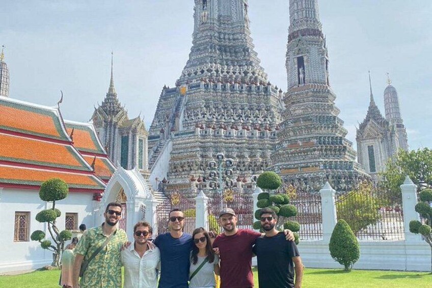 A group of people in front of a large, ornate temple with multiple spires and a white building with a green roof. 3