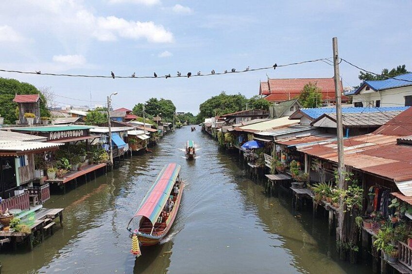 A narrow waterway flanked by houses with red roofs, a long boat with a blue stripe, and a clear sky. 5