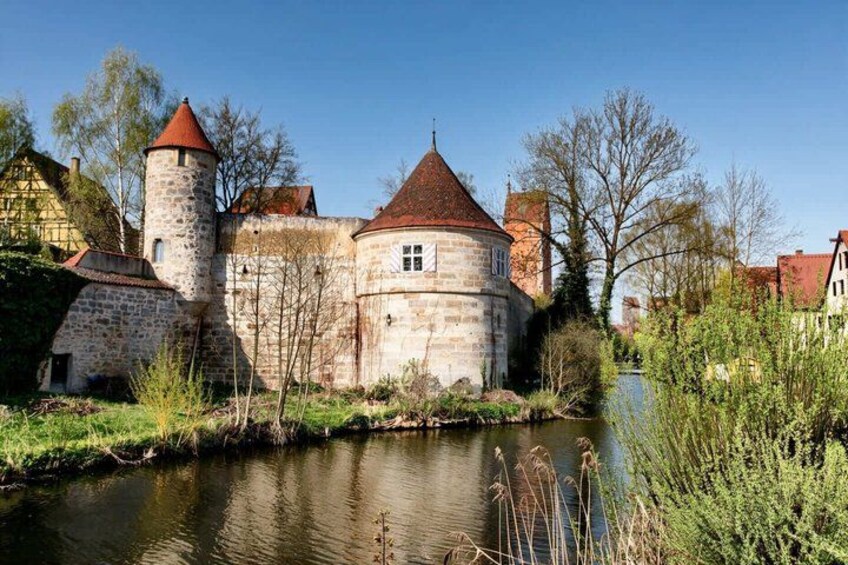 A historic stone castle with a tower, a river, and surrounding greenery. 1