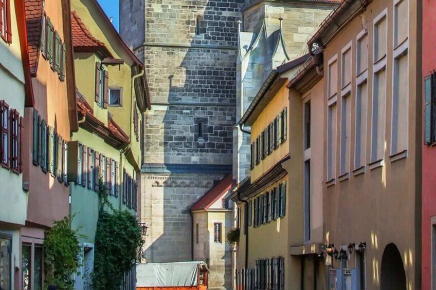 A narrow street with colorful buildings, a stone tower, and a covered bridge. 4