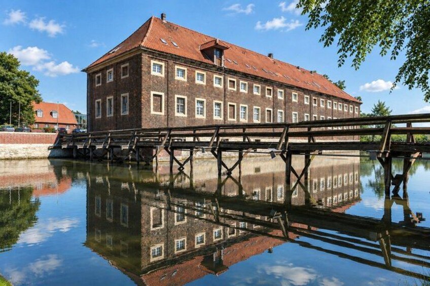 A historic building with a red roof, a wooden bridge over a calm water body, and a clear blue sky. 4