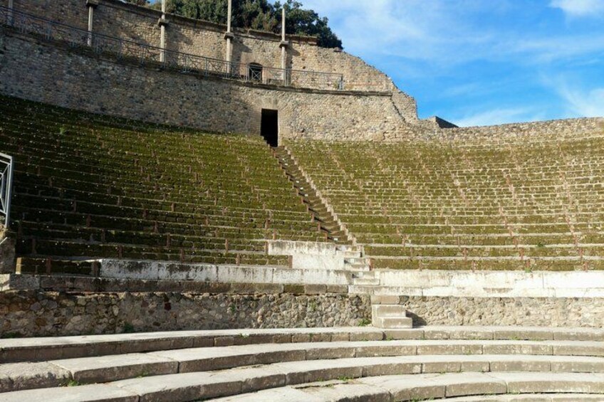 A stone amphitheater with tiered seating and a staircase leading up to the stage. 3