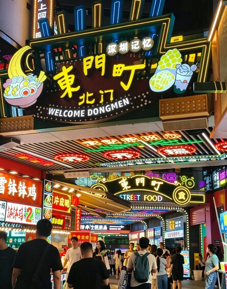 A bustling street food market with neon signs and food stalls. 2