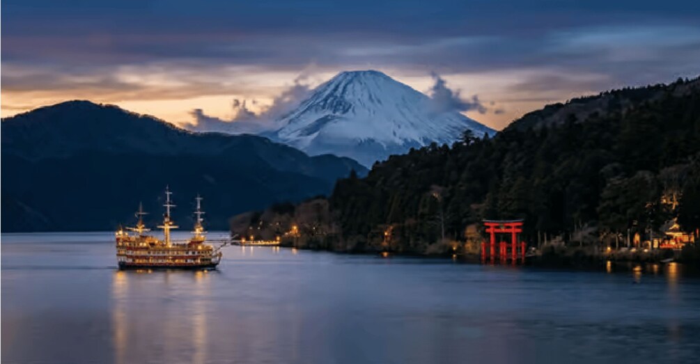 A cruise ship on calm waters with a snow-capped mountain in the background and a red torii gate on the shore. 1