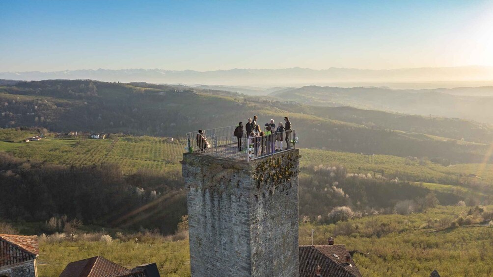 Un groupe de personnes se trouve sur une tour de pierre qui surplombe une vallée, avec des champs et des montagnes lointaines. 1