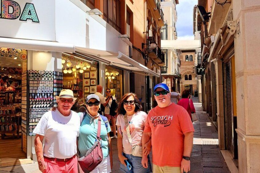 A group of people standing in a narrow street with shops on either side. 4