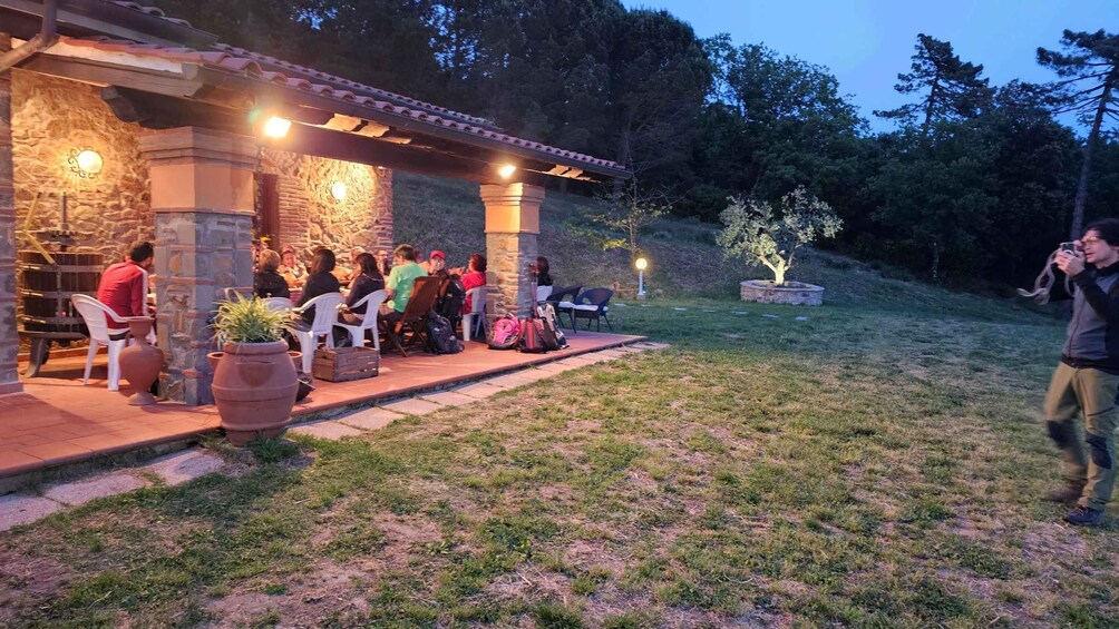 Un bâtiment en pierre avec un toit en tuiles, entouré de pelouse et d’arbres, où des personnes sont assises à des tables à l’extérieur. 4