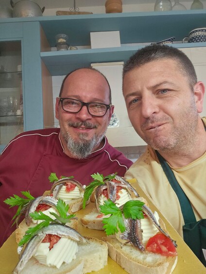 Deux hommes se trouvent dans une cuisine, devant une table où sont disposés des amuse-gueule à base de poisson et de fromage. 2