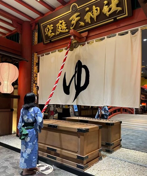 A person in traditional attire standing in front of a large banner with a prominent black symbol. 1