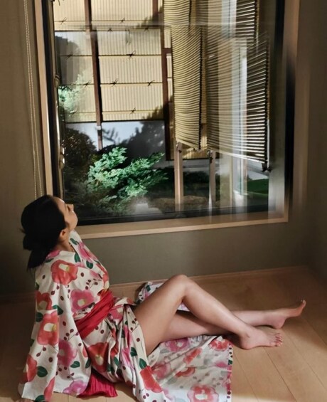 A person sitting by a window with a view of a building and greenery. 2