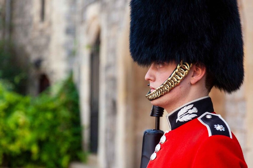 Eine Person in einer roten Uniform mit einem schwarzen Fellhut und Goldverzierungen, die ein Mikrofon hält. 2