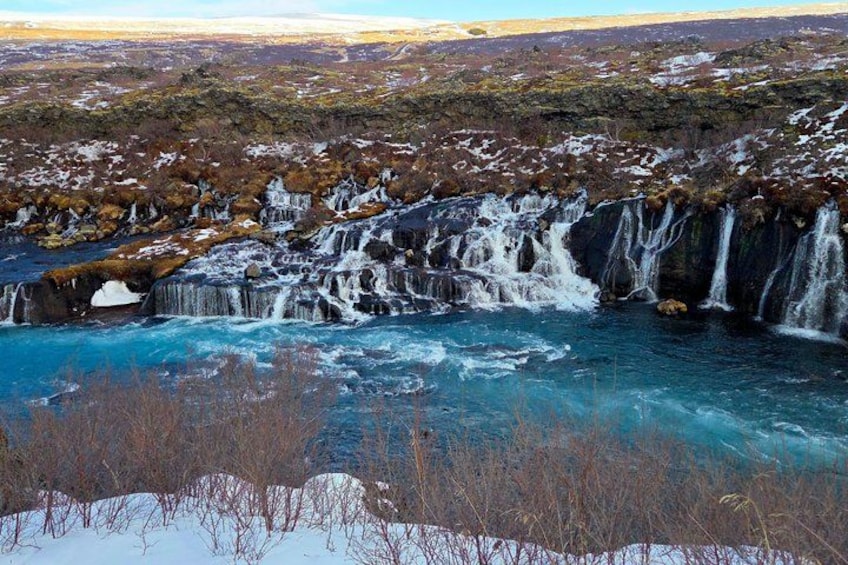 A waterfall cascading over rocks into a river, surrounded by a snowy landscape with sparse vegetation. 4