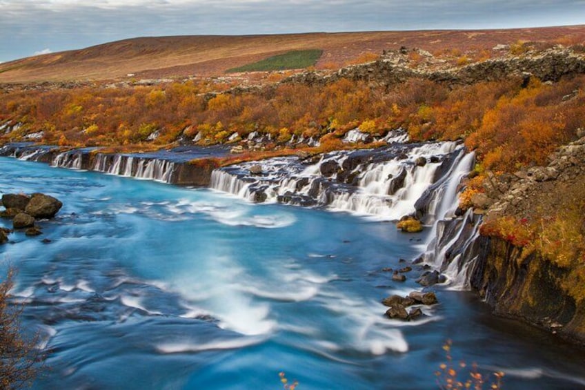 A waterfall cascading over rocks into a river, surrounded by autumn-colored trees. 1