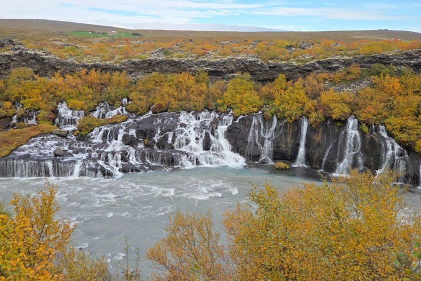 A waterfall cascading over a rocky cliff into a river, surrounded by autumn-colored trees. 5