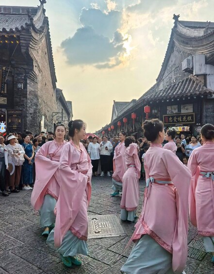 Un groupe de personnes, vêtues de costumes traditionnels, interprète une danse dans une rue historique bordée d’immeubles richement décorés. 2