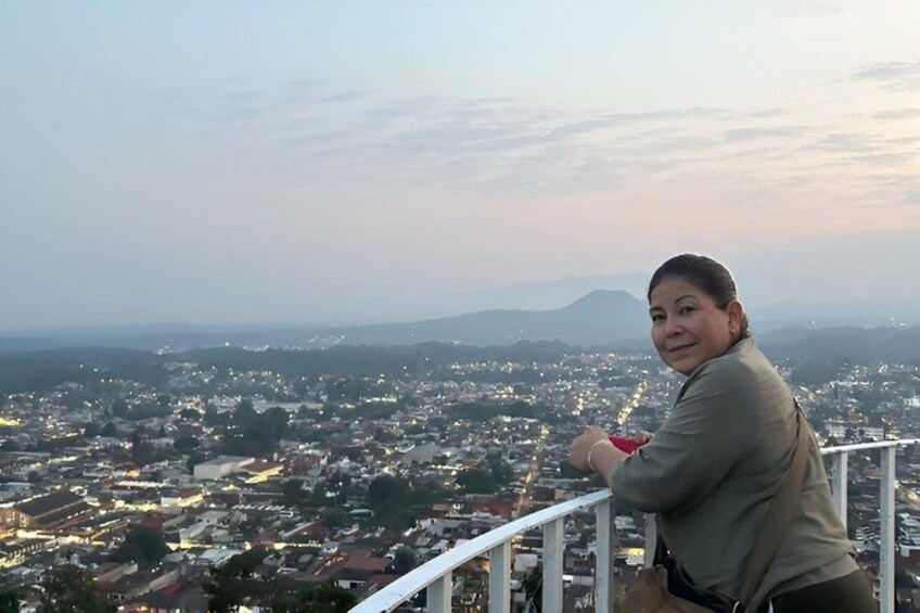 A person standing on a balcony overlooking a cityscape with buildings and distant mountains. 1