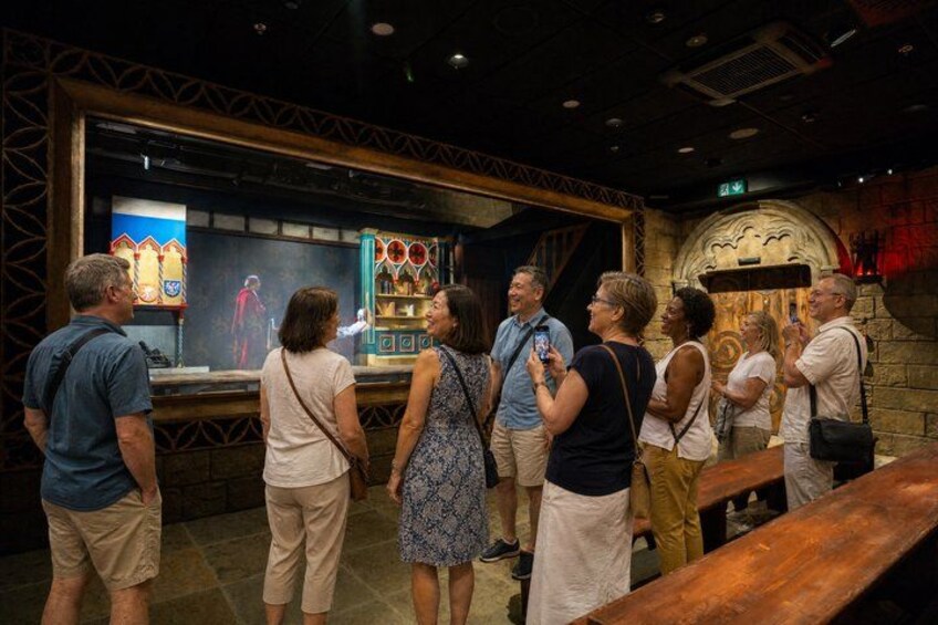 A group of people standing in a museum-like setting with exhibits and a stone wall. 2
