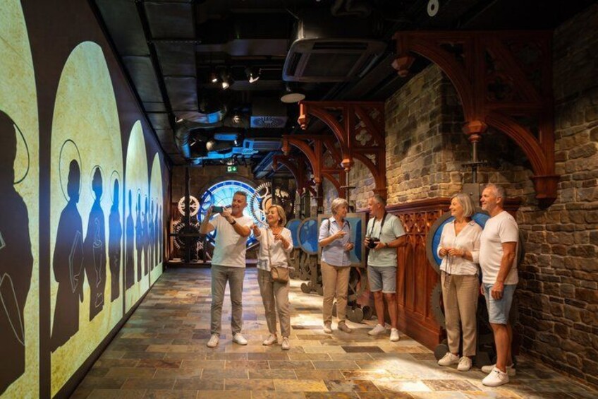 A group of people in a museum corridor with stone walls and wooden arches. 4