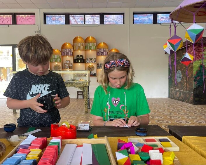 Two children at a table with colorful geometric shapes and a decorative item hanging from the ceiling. 5