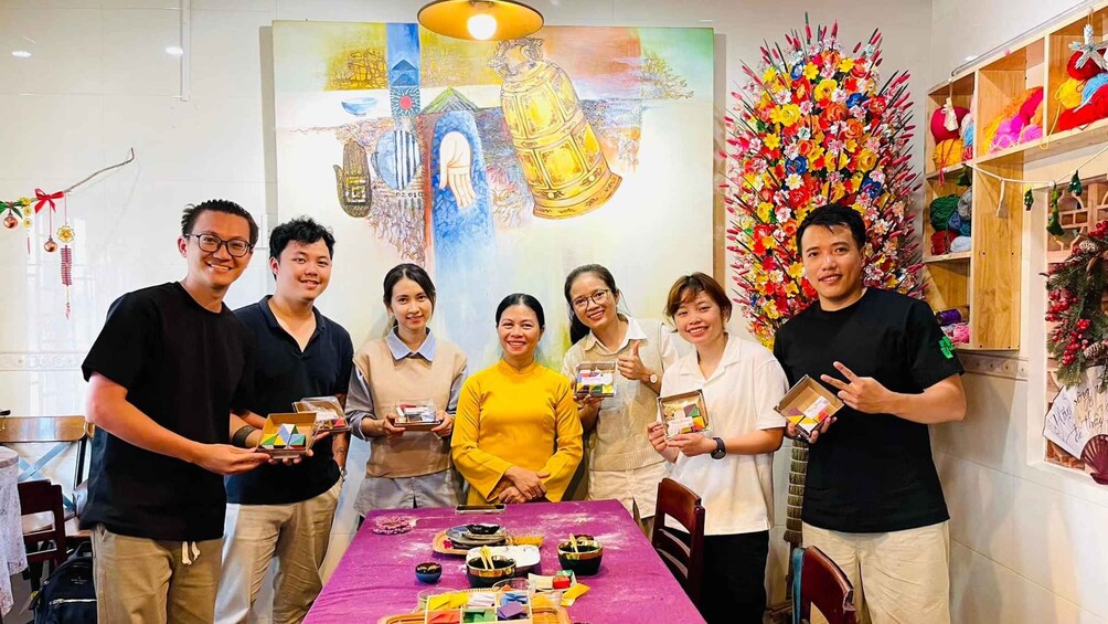 A group of people holding boxes, a table with various items, and a colorful wall decoration. 2