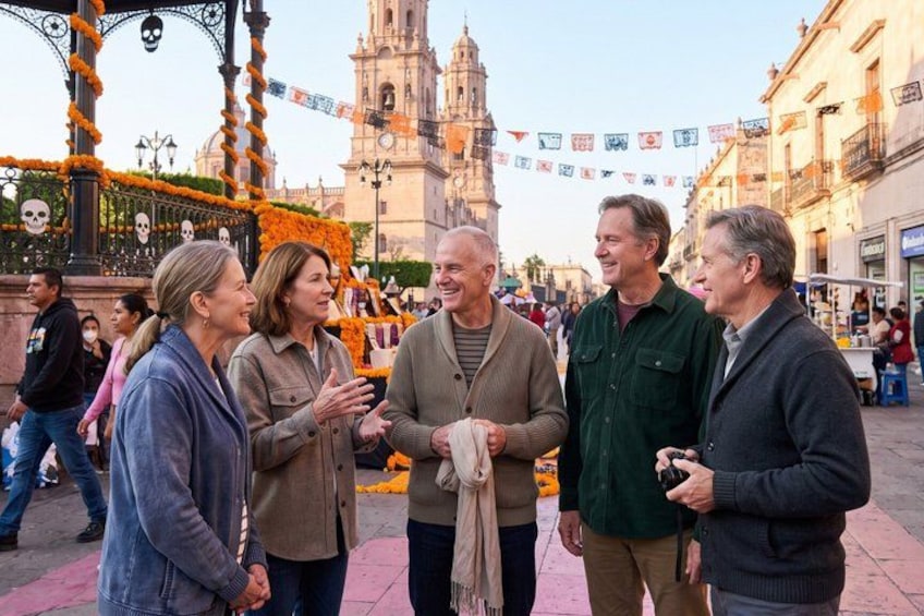 A group of people standing in a public square with a church and a decorative archway in the background. 1