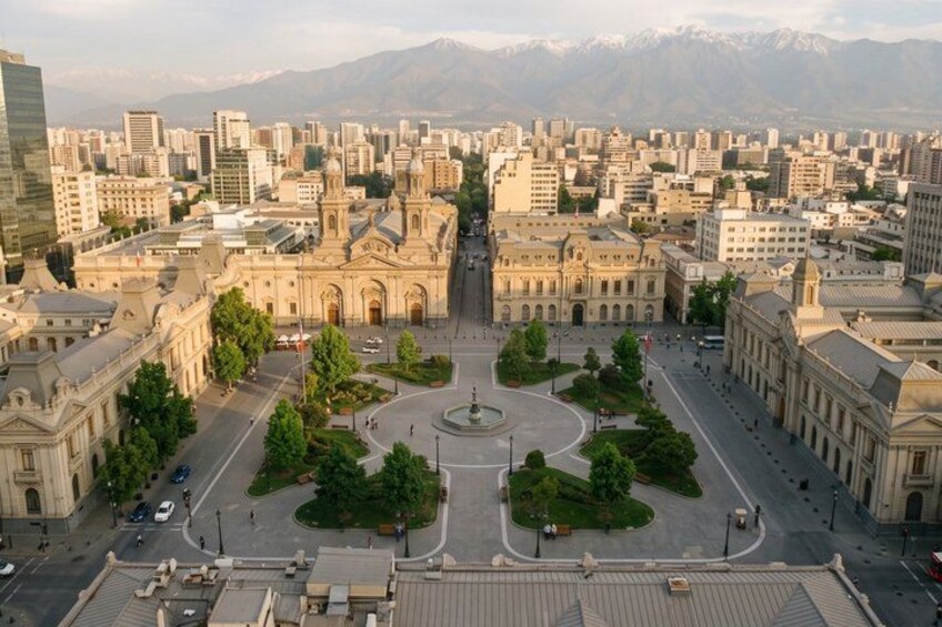 A cityscape with a central roundabout, historic buildings, and a mountainous backdrop. 2