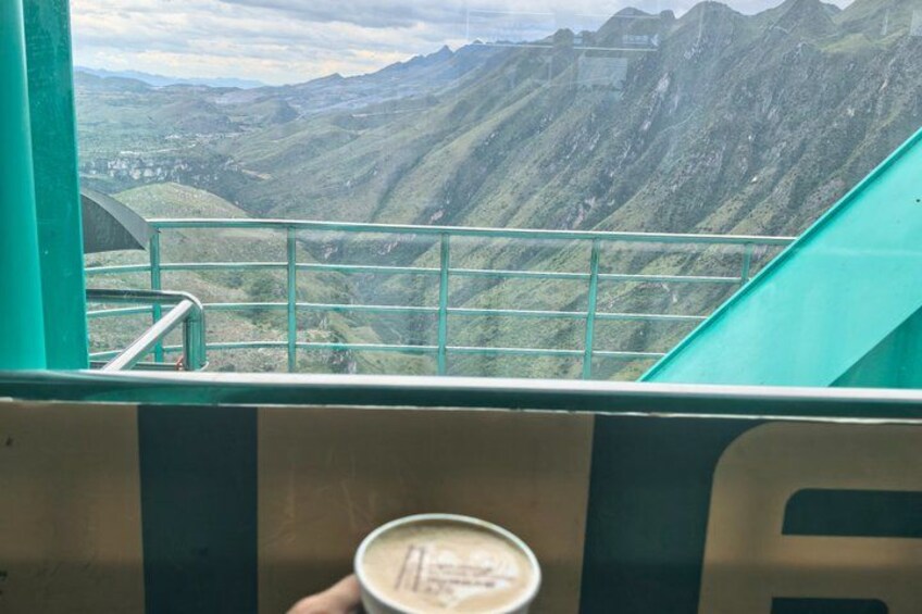 A mountainous landscape with a green railing and a person holding a cup. 5