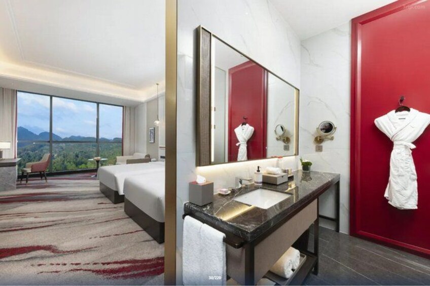 A hotel room with a large bed, a red door, a bathroom with a sink and mirror, and a view of the mountains. 3