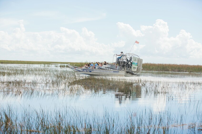 A boat with people on it, moving through a marshy area with water and tall grasses. 4