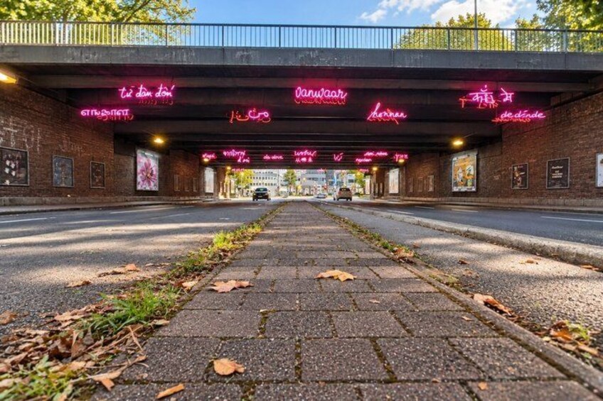 A street under a bridge with neon signs and a brick wall. 5