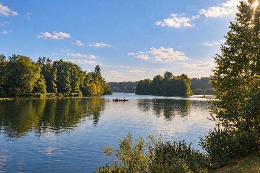 A calm lake with a rowboat, surrounded by dense trees and a clear sky. 2