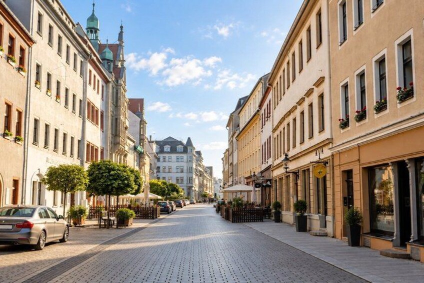 A cobblestone street lined with historic buildings, a church spire, and parked cars. 2