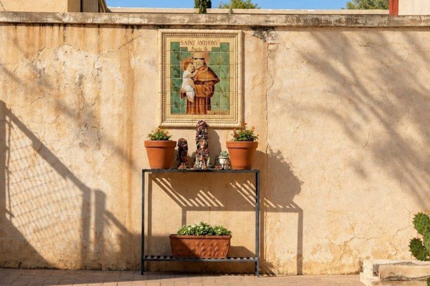 A wall with a religious painting, a metal shelf with potted plants, and a small statue. 2