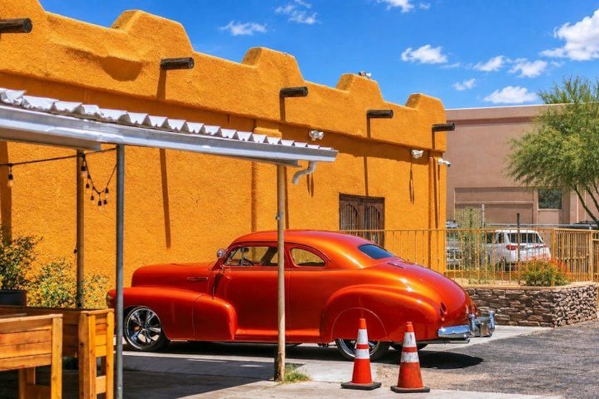 A vintage red car parked in front of a yellow building with a white awning. 3