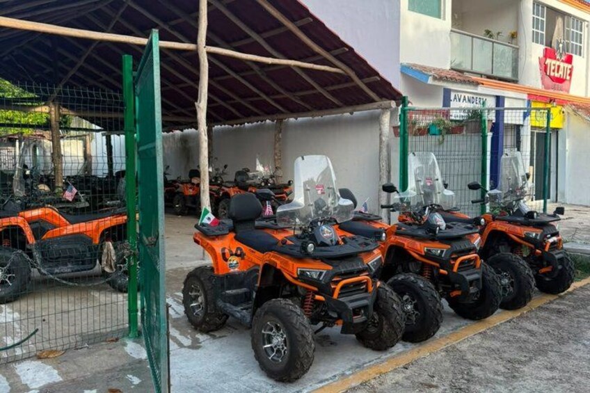 A row of orange ATVs parked under a shelter. 5