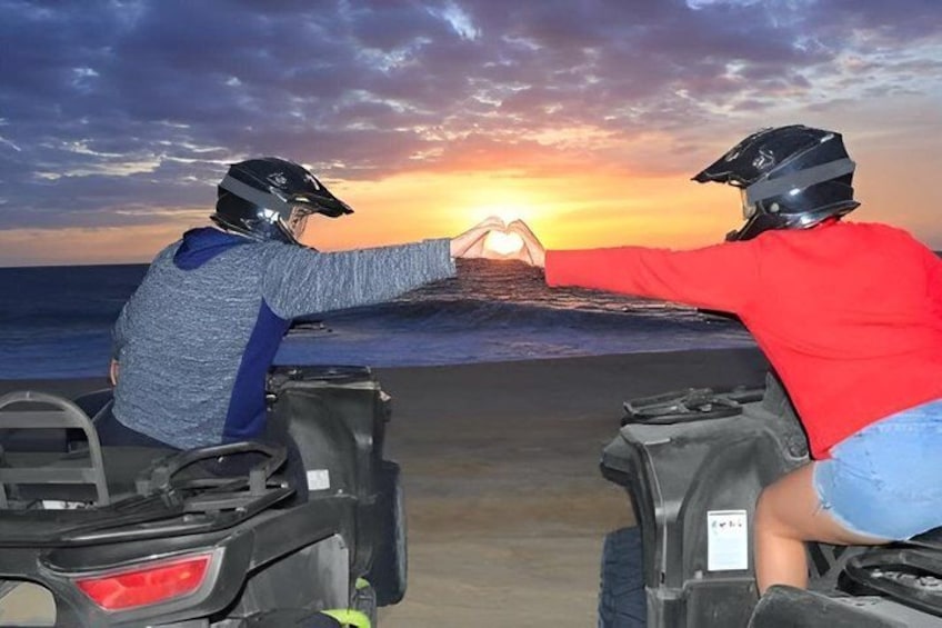 Two people on ATVs at sunset with a heart shape made by their hands. 3