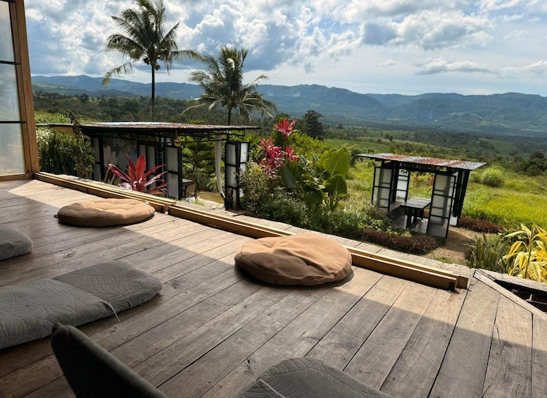 Eine Holzterrasse mit Kissen, umgeben von tropischen Pflanzen und Blick auf Berge. 5