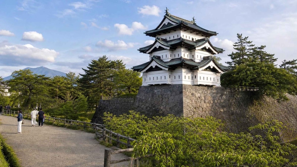 Eine traditionelle japanische Burg mit mehreren Geschossen, umgeben von Grünflächen und einer Steinmauer. 3