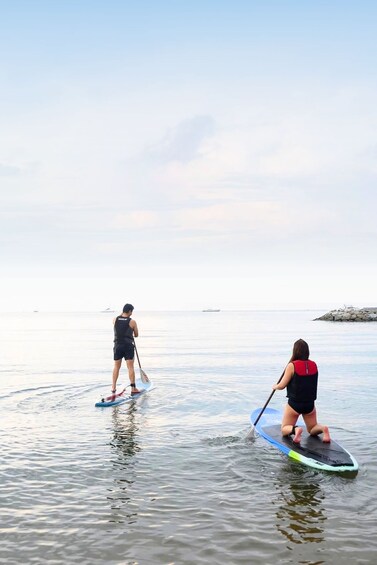 Zwei Personen stehen auf Paddleboards auf ruhigem Wasser unter einem wolkenlosen Himmel. 1