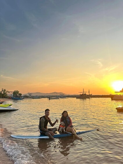 Zwei Personen sitzen auf einem Surfbrett im ruhigen Wasser bei Sonnenuntergang. 4
