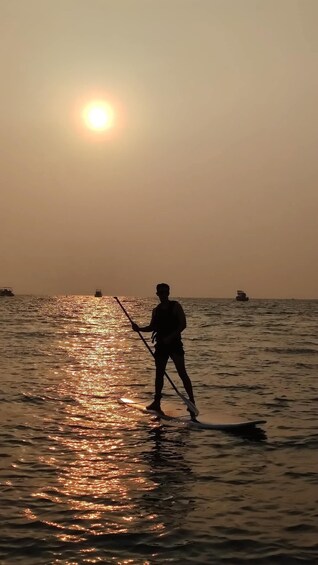 Eine Person steht auf einem Paddleboard auf ruhiger See im Sonnenuntergang. 2