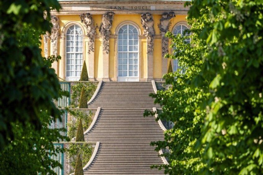 A grand building with a staircase leading up to a large arched entrance, surrounded by lush greenery. 3